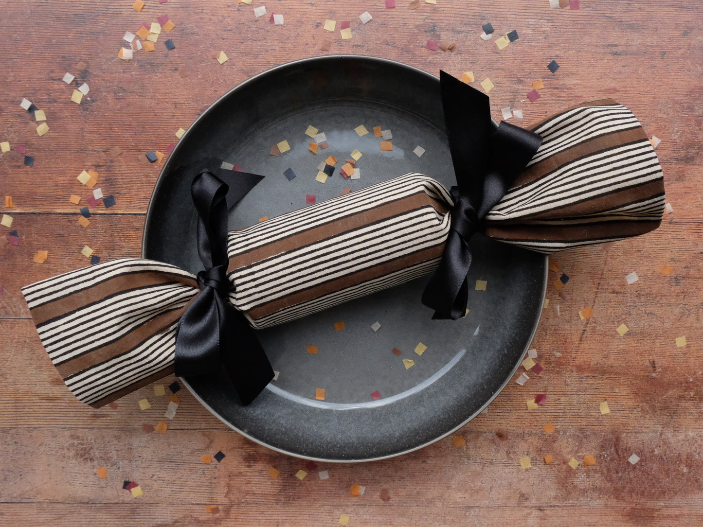 a single stripe print luxury reusable Christmas cracker on a plate surrounded by biodegradable paper confetti sprinkles