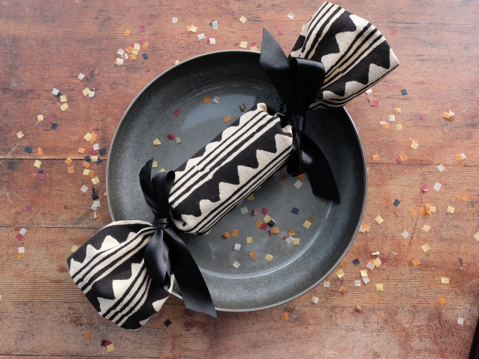 a single peak print luxury Christmas cracker on a plate surrounded by biodegradable paper confetti sprinkles 