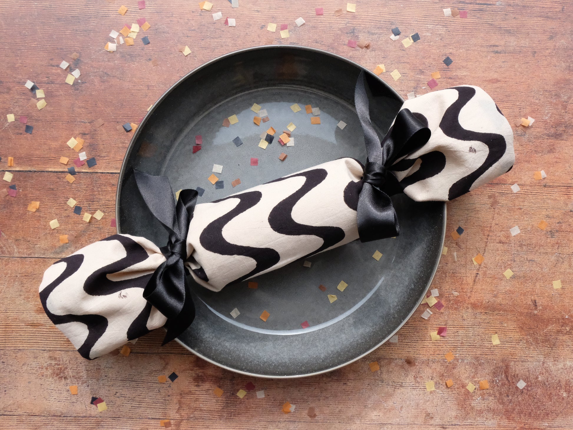 a single luxury Christmas cracker on a plate surrounded by biodegradable paper confetti mini squares 